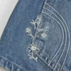 Ultra låg midja, medium tvätt, minishorts i denim med blommig brodyr Ultra låg midja, medium tvätt, minishorts i denim med blommig brodyr
